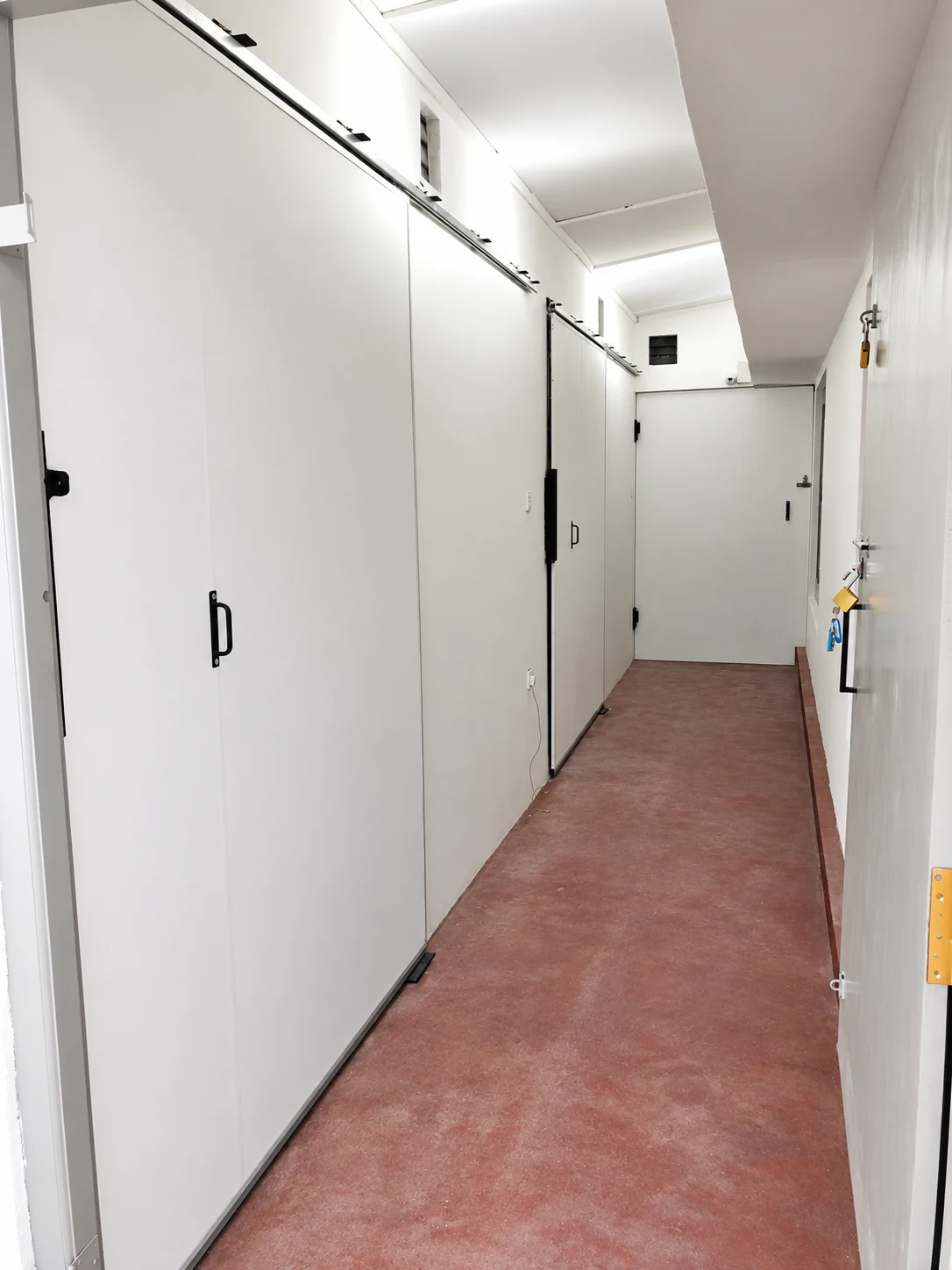 Private storage rooms with individual doors and padlocks along an indoor corridor